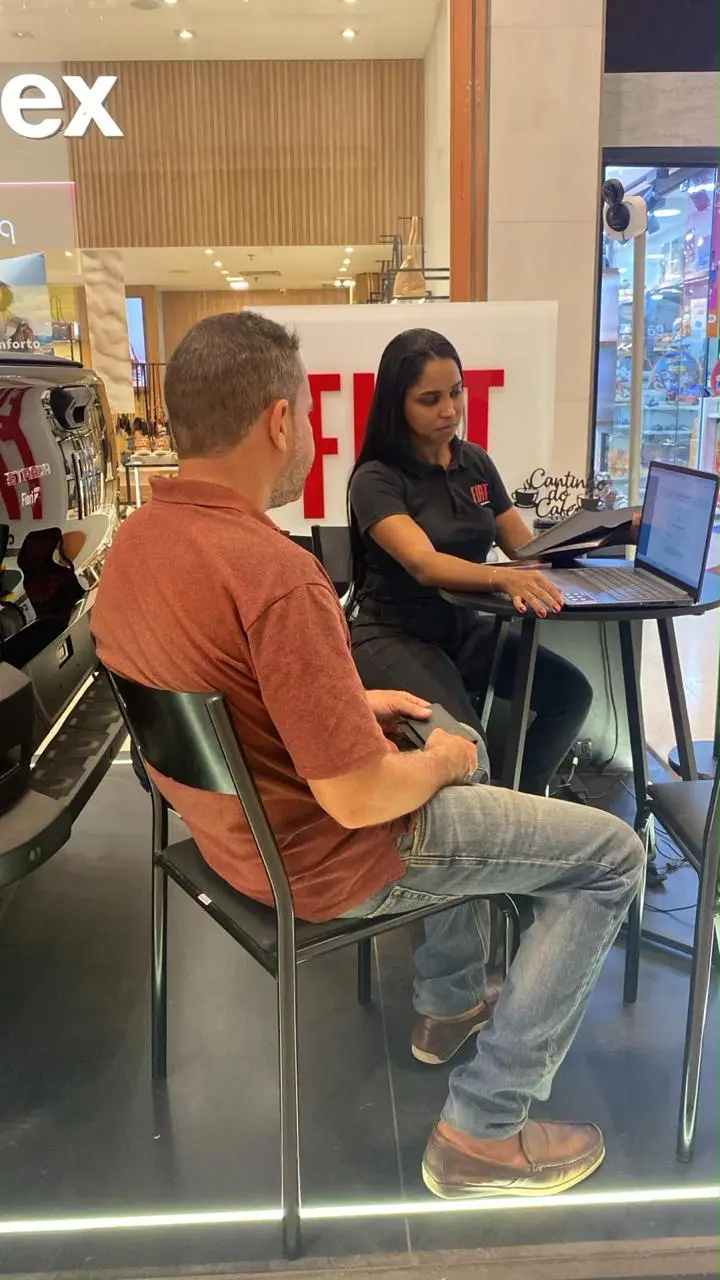 Consultora da ABA atendendo um cliente sentado à mesa do stand, com notebook aberto