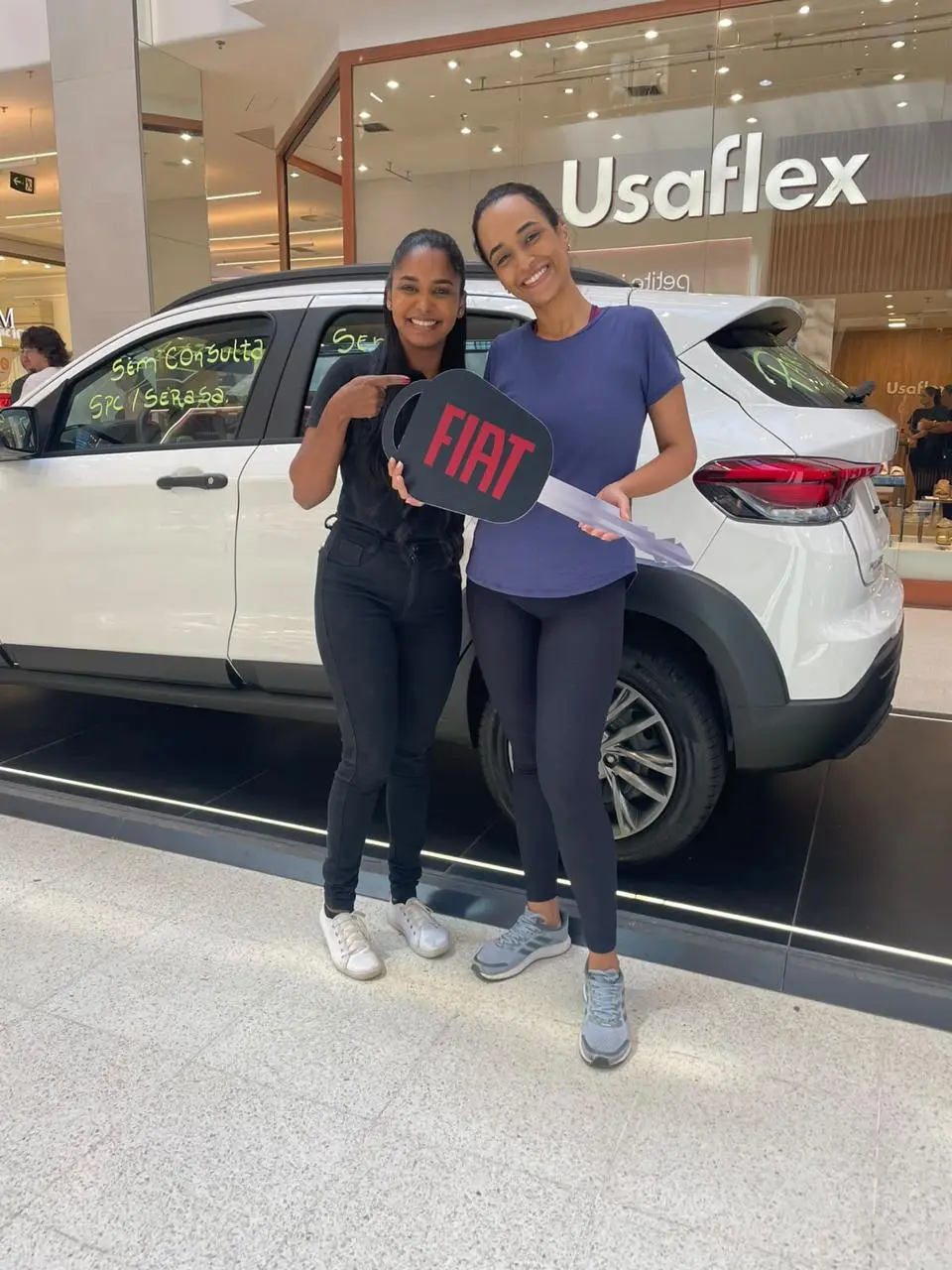 Consultora da ABA e cliente sorrindo com a chave Fiat em frente a um carro branco