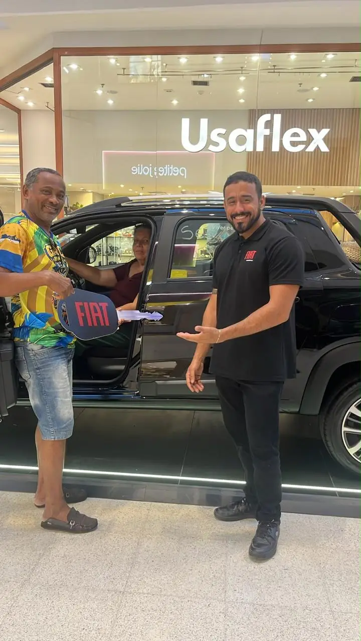 Consultor da ABA de camisa Fiat entregando a chave cenográfica a um cliente ao lado de uma picape preta
