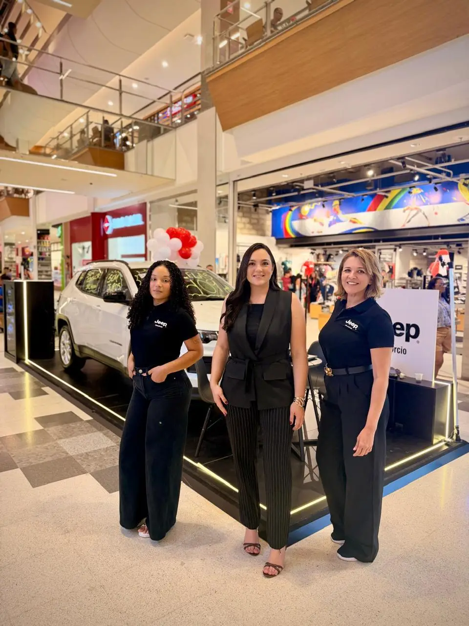 Três consultoras da ABA em frente ao stand Jeep, com um Jeep branco ao fundo